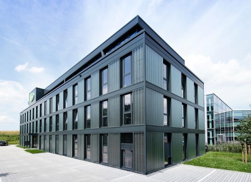 Moderne Bürogebäude mit Glasfassade und klaren Linien, umgeben von Bäumen und einem Gehweg