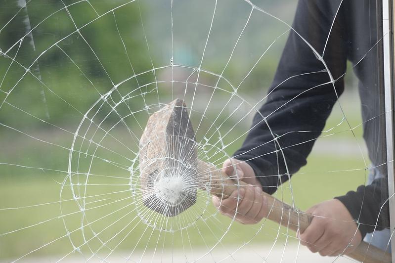 Ein Mann hält einen Hammer und zerbricht ein Glasfenster