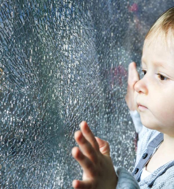 Kleinkind steht vor einer kaputten Fensterscheibe